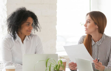Multiracial male and female colleagues discussing document at team meeting or corporate office briefing, diverse friedly african and caucasian partners talking about contract at group negotiations