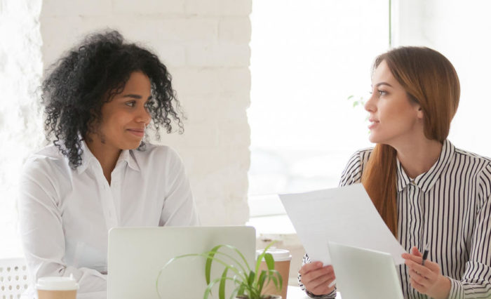 Multiracial male and female colleagues discussing document at team meeting or corporate office briefing, diverse friedly african and caucasian partners talking about contract at group negotiations