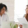 Multiracial male and female colleagues discussing document at team meeting or corporate office briefing, diverse friedly african and caucasian partners talking about contract at group negotiations
