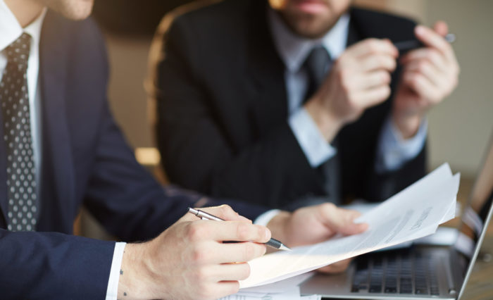 Closeup portrait of two unrecognizable  business partners reviewing paperwork and signing contract papers at table during meeting