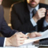 Closeup portrait of two unrecognizable  business partners reviewing paperwork and signing contract papers at table during meeting